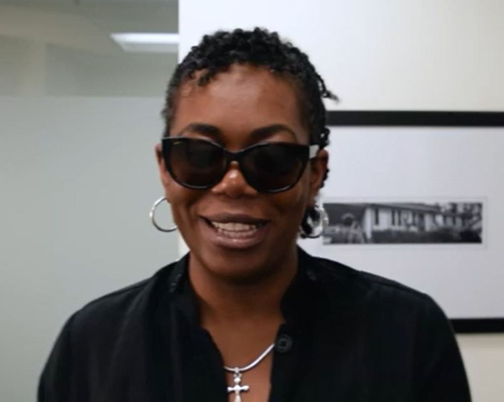 Justice in a black jacket smiling directly into the camera with black sunglasses.